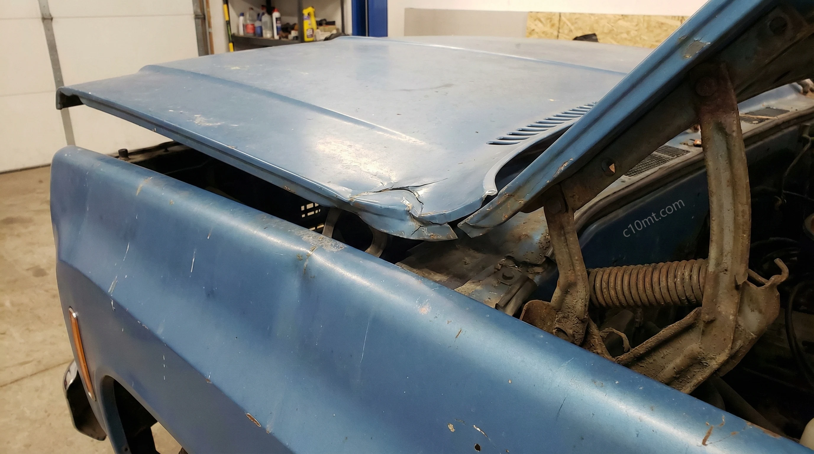 Close up of a buckled Chevrolet C10 hood near the hinges showing the classic hood kink