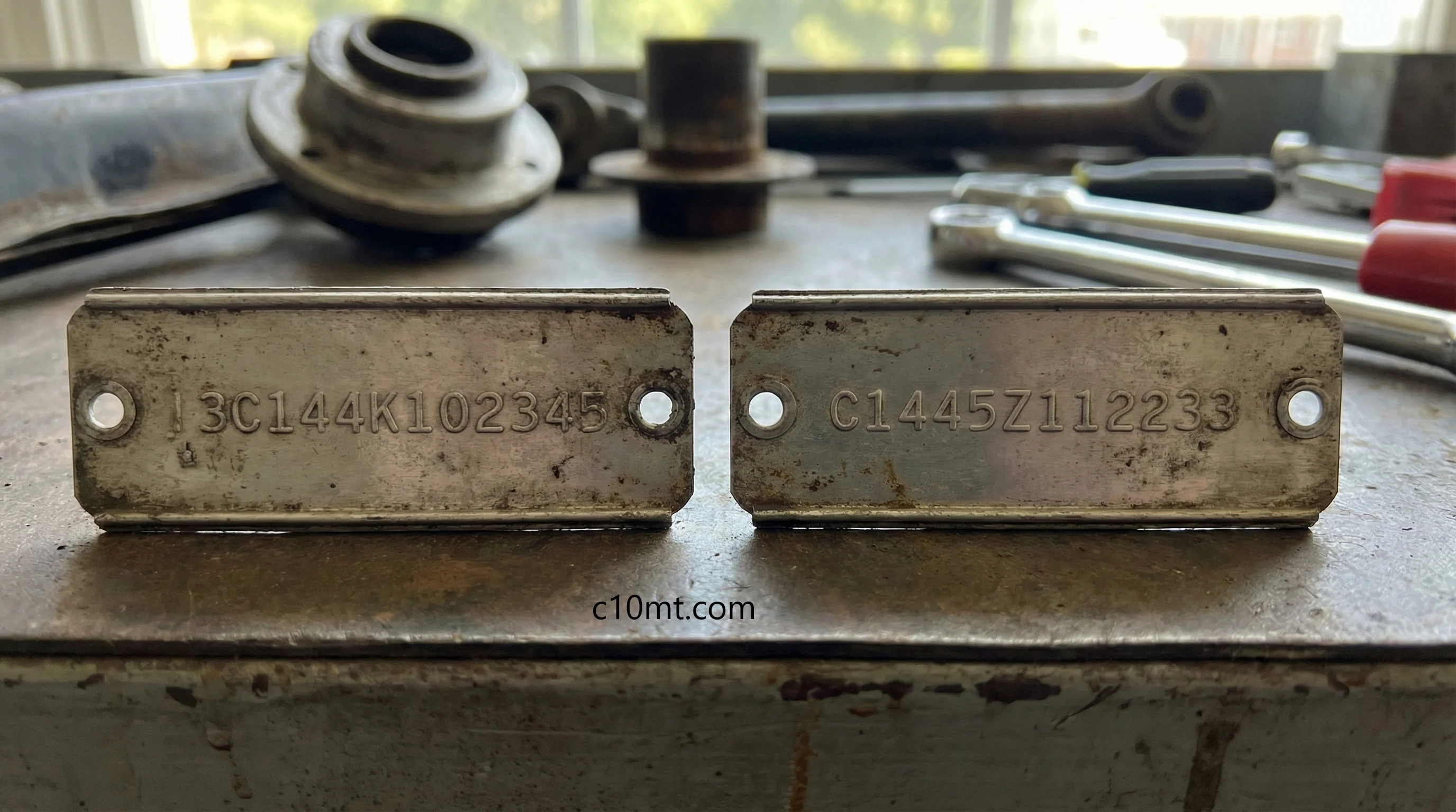 Side-by-side comparison of two weathered Chevrolet C10 VIN plates on a workbench, illustrating the syntax shift between the 1960–1963 'year-first' format and the 1964–1966 'chassis-first' format.